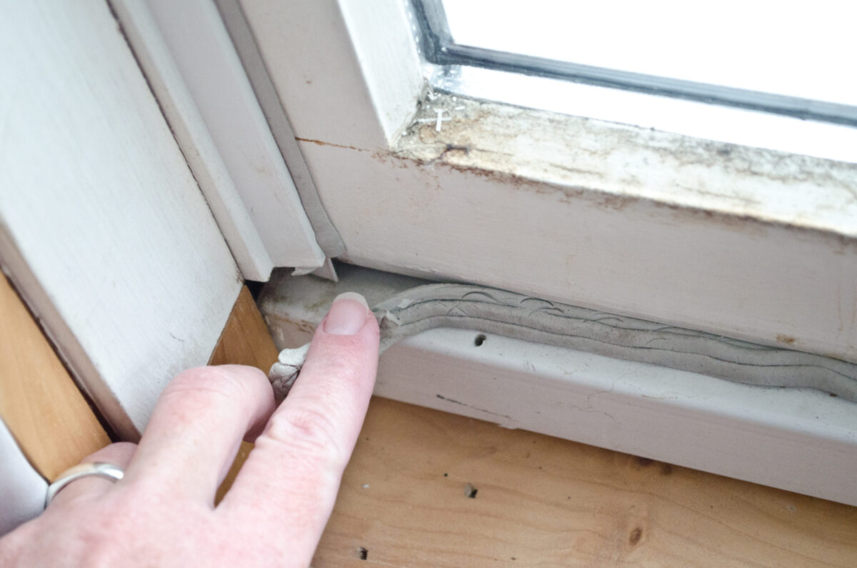 Woman's hand pulling back detached weather stripping from window seal